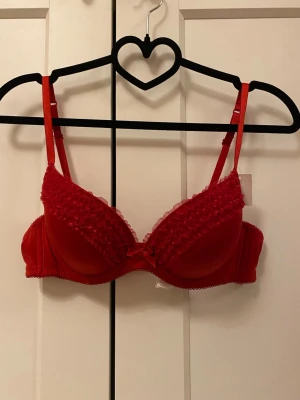 Röd bh med volang från Lindex 80B - Snygg röd bh från Lindex i storlek 80B. Bh:n har volangdetaljer på kuporna och en liten rosett framtill. Axelbanden är justerbara.💕