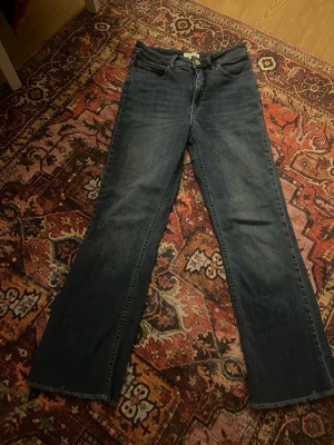 blå bootcut jeans - Snygga ljusblå jeans med bootcut-snitt och klassisk femficksdesign. Jeansen har en lätt tvättad look och rå kant längst ner på benen för en cool vibe. Perfekta för dig som gillar en lite bredare passform nertill och vill ha en tidlös stil.