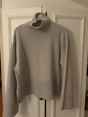 Ljusgrå polotröja i ull/kashmir - Säljer en ljusgrå polotröja i mjuk ull- och kashmirblandning. Tröjan har bred ribbad kant vid hals, ärmslut och nederkant samt lång ärm. Perfekt för kyliga dagar och har en loose passform som ger en chill vibe.