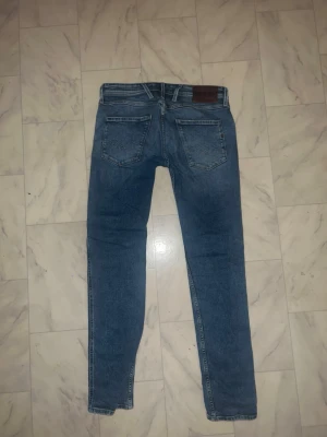 Replay blå jeans med slitningar - Säljer ett par snygga Replay jeans i klassisk blå  med slitningar. Storlek 30W 32L. Skriv vid funderingar