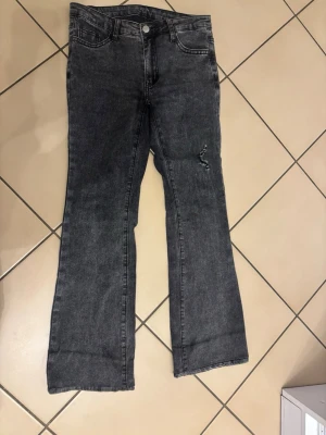 Bootcut svarta jeans med slitning - Snygga svarta bootcut jeans med en lätt slitning på ena benet. Klassisk femficksmodell och knappstängning fram. Jeansen har en mörk tvätt och är tillverkade i jeansmaterial med lite stretch för skön passform.