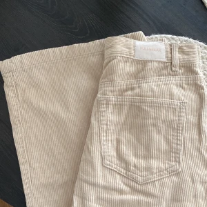 Beiga manchesterbyxor Pull&Bear 36 - Snygga beiga manchesterbyxor från Pull&Bear i storlek 36. Byxorna har hög midja, raka ben och klassisk femficksmodell. Tillverkade i mjuk manchester med dragkedja och knapp framtill. 