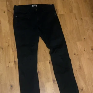 Svarta Wrangler Greensboro jeans W32 L32 - Svarta jeans från Wrangler, modell Greensboro, med klassisk femficksdesign och raka ben. Jeansen har normal passform och är tillverkade i ett slitstarkt bomullsmaterial. Perfekta för dig som gillar en clean och tidlös look.