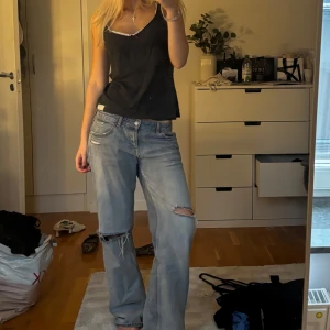 Odd Molly Linné - Säljer en svart ribbad linnetopp med smala axelband och vit spetskant längs urringningen. Toppen har en liten röd rosett framtill som detalj och är i mjukt, stretchigt material. Perfekt att styla med jeans eller kjol för en chill look.