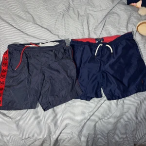 2 st badbyxor från moncler och polo - Säljer ett par marinblå badshorts från Polo Ralph Lauren med röd insida och vit snörning i midjan. Shortsen har klassisk passform och är tillverkade i polyester, perfekt för sommaren. Diskret Polo-logga broderad i rött på benet. Snygga och stilrena för stranden!