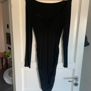 Svart långärmad tight klänning - Svart långärmad klänning med tight passform och rynkade detaljer vid bysten. Klänningen har en djup, något v-ringad halsringning och är tillverkad i ett stretchigt material som sitter snyggt på kroppen. 