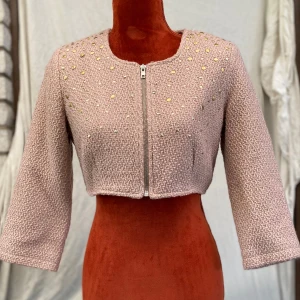Vila Ljusrosa croppad cardigan jacka med nitar M - Superfin ljusrosa croppad cardigan jacka med trekvartsärm och dragkedja framtill. Jackan har ett stickat utseende och är dekorerad med små guld- och silverfärgade nitar upptill. Fodrad med mjukt tyg på insidan för extra komfort. ﻿64% polyester ﻿17% viskos ﻿11% akryl ﻿8 % bomull ﻿Foder: 100% polyester ﻿Längd: 37 cm ﻿Bystvidd: 46 cm.   Inga bilder när den sitter på mig! Katter finns i hemmet!