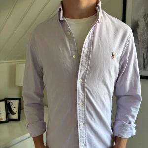 Ljuslila skjorta från Ralph Lauren - Säljer en stilren ljuslila skjorta från Ralph Lauren i slim fit. Skjortan har klassisk krage och tillverkad i mjuk bomull. Skjortan pasar lika bra till fina tillfällen som tillvardags. Killen på bilden är 178. 