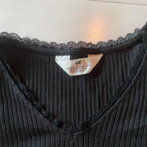 Svart ribbad långärmad topp - Svart ribbad långärmad topp från H&M med v-ringning och spetskant vid halsen i storlek 158/164💕 Jag har använt den ungefär 4-5 gånger men säljer för jag tyckte att den var lite för kort för mig💞 Den ser ganska skrynklig ut på bilden, men det är för att armarna skulle få plats i bilden, så den är alltså inte skrynklig på. 💘😇