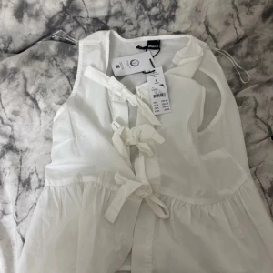 Vit ärmlös klänning från Pieces - Supersöt vit klänning från Pieces med knyt framtill och ärmlös design. Lätt och luftig bomull, perfekt för varma dagar. Stilren och enkel med fina detaljer som ger en trendig vibe.