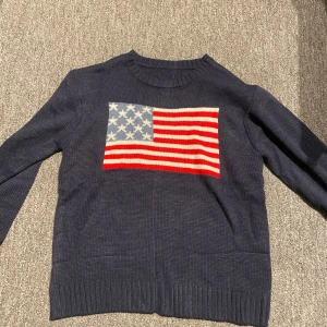 Mörkblå stickad tröja med USA-flagga - Snygg mörkblå stickad tröja med en stor amerikansk flagga på bröstet. Lite pösig vid armarna, passar 150-164