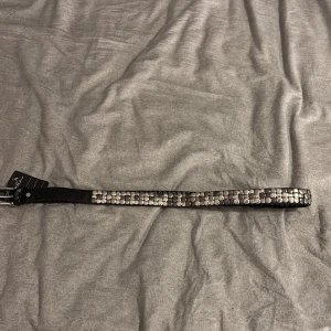 Svart nitarbälte i äkta skinn - Snyggt svart bälte i äkta skinn med massor av silvriga runda nitar längs hela bandet. Bältet har ett coolt, rockigt uttryck och ett rejält silverspänne. Perfekt accessoar för att lyfta din outfit med lite extra edge.