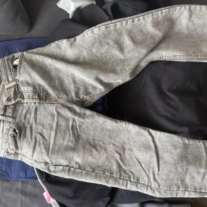 Grå jeans från Montén, storlek 30/32 - Säljer ett par grå jeans från Montén med snygga kontrastsömmar och klassiska bakfickor med unik zigzag-detalj. Jeansen har en cool, lite tvättad look och en grön patch bak i midjan som sticker ut. Perfekt för dig som gillar streetstyle.