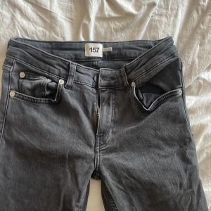 Grå jeans low bootcut från 157 - Snygga grå jeans från 157 med low bootcut-passform. Klassisk femficksmodell med dragkedja och knapp i midjan. Jeansen har en mörkgrå tvätt och raka ben med lätt utsvängd nederdel. Perfekta för en avslappnad och trendig look.