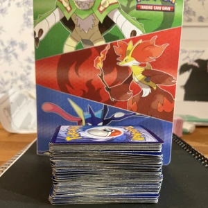 Pokémon Trading Card Game - Samlarpärm med färgstarka Pokémon-motiv och en stor bunt Pokémonkort. Runt 150 kort i högen med ett antal GX:ar. Korten är ansvällda men i fint skick, premien är ganska sliten men fungerar även den