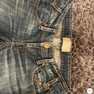Blå Replay jeans med detaljer - Snygga blå low waist Replay jeans med slitningar och coola nitar på bakfickorna. Klassisk femficksmodell med raka ben och kontrastsömmar. Jeansen har bälteshällor och en unik bakre spänndetalj. Perfekta för dig 