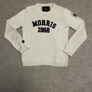 Vit tröja från Morris - Snygg vit tröja från Morris med svart text 'Morris 1968' på bröstet. Tröjan är tillverkad i 100% bomull och har också en logga på vänster arm. Grövre stickad som ger en snygg textur och bra passform. Inga defekter och knappt använd. Storlek M