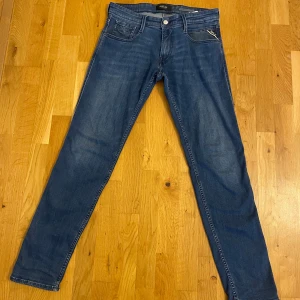 Blå jeans från Replay - Snygga blå jeans från Replay med klassisk femficksdesign och raka ben. Jeansen har en slim fit passform och är tillverkade i mjukt denimtyg med diskreta slitningar för en cool look. Perfekta för dig som gillar stilrena och tidlösa jeans.                                                              Strl 30/32.                                                                             Knappt använda/ mycket bra skick                                                                  Nypris 1199kr