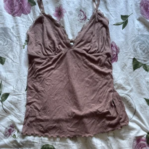 Ljusbrun ribbad linnetopp från Index - Supersöt ljusbrun ribbad linnetopp från Index med spetsdetaljer längs v-ringningen och tunna axelband. Toppen har vågig kant nertill och är tillverkad i mjuk viskosblandning. Perfekt för lager-på-lager eller sommarens varma dagar.