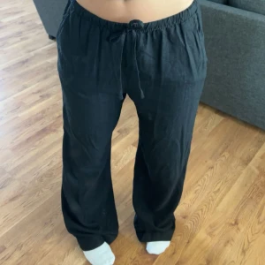 Svarta vida linnebyxor med snörning - Säljer ett par svarta linnebyxor med bred passform och dragsko i midjan. Byxorna har hög midja och är riktigt sköna och luftiga, perfekta för chill dagar. Materialet är linne och de har en loose fit som ger en avslappnad vibe. Använt 1 gång!