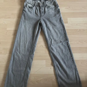 Grå raka jeans från Denim Day - Grå jeans från Denim Day i rak modell med klassiska fem fickor och bälteshällor. Jeansen har en enkel design och är tillverkade i denim med knapp och dragkedja framtill. Perfekta för dig som gillar en clean och avslappnad look.