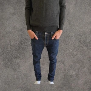 Nudie Jeans blå jeansbyxor W31 L32 - Snygga blå jeansbyxor från Nudie Jeans med klassisk femficksdesign och orangea sömmar. Byxorna har normal passform och raka ben, tillverkade i slitstarkt bomullsjeans. Perfekta för dig som gillar stilrena och tidlösa jeans.