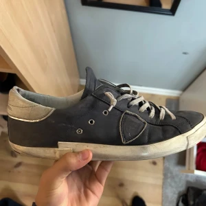 Ett par feta Philippe Model i blå! - Snygga sneakers från Philippe Model i mörkblå skinn med ljusgrå detaljer och snörning. Skorna har en vit sula med svarta undersidor och klassisk låg profil. Perfekta för dig som gillar stilrena och exklusiva sneakers med en urban vibe.