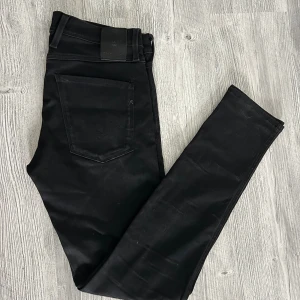 Svarta Replay Anbass jeans herr - Svarta Replay Anbass jeans med klassisk femficksdesign och diskreta svarta detaljer. Jeansen har normal passform och raka ben, tillverkade i stretchig bomullsblandning för extra komfort. Snygg Replay-logga på bakfickan och läderpatch i midjan.