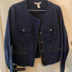 Mörkblå overshirt från NLY Trend - Snygg mörkblå overshirt från NLY Trend i storlek 40. Jackan har rund hals, två bröstfickor med knappar och två fickor med dragkedja framtill. Långärmad och tillverkad i bomull. Den har lite fjun på sig eftersom som det inte varit använd mycket och mest hängt i garderoben, kommer tvätta den så de är inga problem om att fråga om bilder efter tvätt. Den är använd ett par fåtal gånger! 
