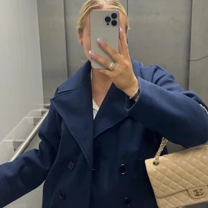 Mörkblå rock med bred krage - Snygg mörkblå rock med bred krage och dubbelknäppning framtill. Jackan har en klassisk, loose passform och långa ärmar. Perfekt för dig som gillar stilrena och tidlösa plagg med lite extra attityd.