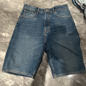 Loose jeansshorts från H&M - Blå jeansshorts från H&M i loose fit med justerbar midja. Klassisk femficksmodell med raka ben och normalhög midja. Perfekta för en chill sommarstil och funkar till allt. Snygg denim med kontrastsömmar och enkel design.
