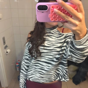 Zebramönstrad stickad tröja - Säljer en stickad tröja med zebramönster i svart och vitt. Tröjan har hög hals, cut out-detaljer vid axlarna och är långärmad. Modellen är lite loose och passar perfekt om du gillar djurmönster och vill sticka ut.