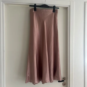 Långkjol i satin, ljusrosa - Snygg och flowy långkjol i ljusrosa satin med lätt glansig finish. Kjolen har en enkel, stilren design och faller fint längs benen. Perfekt för dig som gillar en feminin och elegant look.