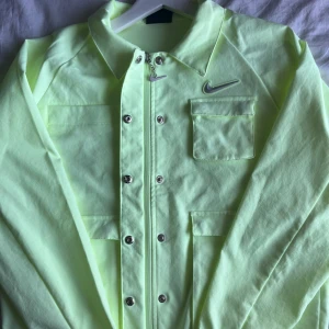 Neongul overshirt från Nike - Nike overshirt i neongult, fyra fickor framtill och silverfärgad dragkedja. Jackan har långa ärmar med resår vid handlederna och snyggt Nike Swoosh-märke på bröstet. I storlek S☺️