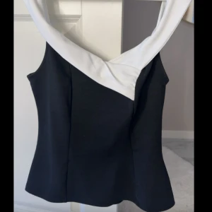 Svart och vit axelbandslös topp - Snygg svart topp med bred vit kant längs den axelbandslösa urringningen. Toppen har en figurnära passform och är perfekt för dig som gillar stilrena kontraster. Materialet känns mjukt och stretchigt, vilket gör den bekväm att bära.