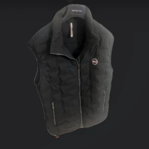 Colmar Väst (Svart)  - Säljer en svart dunväst från Colmar Originals med hög krage och dragkedja framtill. Använt några gånger under en vinter men finns inga defekter. Västen har två fickor med dragkedja och en diskret logga på bröstet. Perfekt att slänga över en hoodie eller t-shirt för en clean look.
