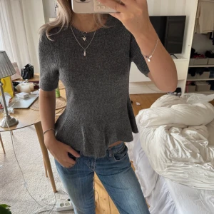 Mörkgrå stickad peplum topp - Superfin mörkgrå stickad peplum topp med kort ärm och volang nertill. Sitter tajt över midjan och ger en snygg siluett. SÄLJER ÄVEN PÅ VINTED OM MAN VILL HA BILLIGARE FRAKT!!