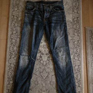 Blå jeans från Nudie Jeans - Blå jeans med riktigt snygg tvätt från Nudie Jeans. Storleken 30/32. Har ett hål vid högra knäet och en liten slitning där bak. 