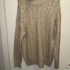 Beige stickad polotröja med flätmönster - Beige stickad polotröja med snyggt flätmönster framtill och på ärmarna. Tröjan har en hög polokrage och långa ärmar med ribbade muddar. Perfekt för dig som vill ha en mysig och stilren look under kyliga dagar.