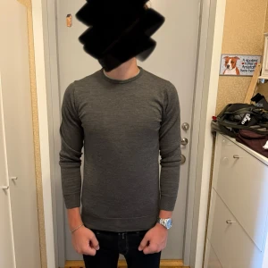 Mörkgrå merinoulltröja Lawrence Grey - Säljer en stilren mörkgrå tröja från Lawrence Grey i merinoullmix. Tröjan har rund halsringning, lång ärm och en clean, klassisk look som funkar till allt. Materialet är 50% merinoull och 50% akryl för både värme och mjuk känsla.