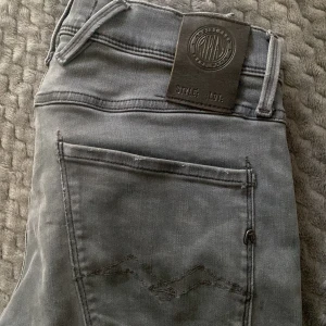 Replay jeans - Säljer ett par grå jeans från Replay med klassisk femficksdesign och snygga detaljer på bakfickan. Skick 10/10. 27/32.