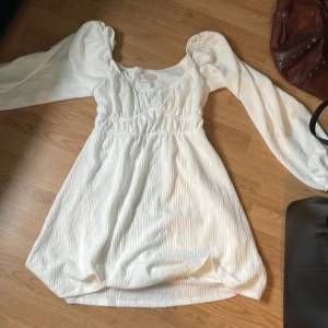 Vit kortklänning från Nelly med puffärm - Supersöt vit kortklänning från Nelly med långa puffärmar och smockad midja. Klänningen har en lätt strukturerad yta och en feminin, romantisk look. Perfekt för dig som gillar trendiga och stilrena plagg med det lilla extra har endast använt denna klänning en gång och har inga fläckar eller defekter😊. Skriv för frågor💗