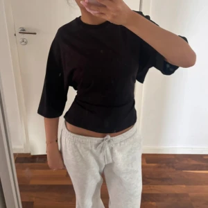 Svart croppad topp med knyt i ryggen - Svart croppad topp med trekvartsärm och snygg knytning i ryggen. T-shirten har en loose passform och är tillverkad i mjukt bomullstyg. Perfekt för dig som gillar en enkel men trendig look.