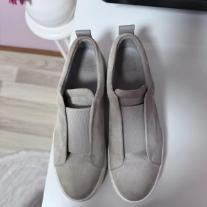 Gråa sneakers i mocka från K.Cobler - Snygga beige sneakers från K.Cobler i mjuk mocka med bred resår över vristen för enkel påtagning. Skorna har en chunky vit platt sula och rund tå. Perfekta för dig som gillar stilrena och bekväma skor med modern känsla. Pris kan diskuteras, kvitto och skolådan finns med. Änvända denna sommar 