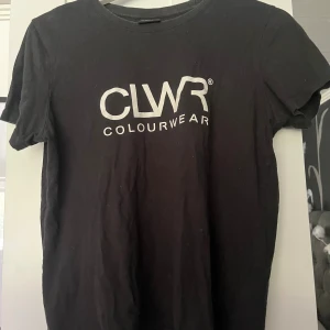 Svart t-shirt från CLWR Colourwear - Svart t-shirt från CLWR Colourwear med vit logga tryckt framtill. Klassisk rund halsringning och korta ärmar. Tillverkad i mjuk bomull som känns skön mot huden. Perfekt för en clean och stilren look.