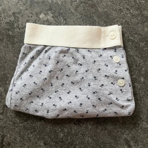 Grå blommiga shorts med knappar - Snygga grå shorts med små mörkblå blommor och vit bred midja. De har tre vita knappar framtill som detalj och är tillverkade i mjuk bomull. Passformen är normal och de är perfekta för chill dagar. Enkla att matcha med en t-shirt eller hoodie.
