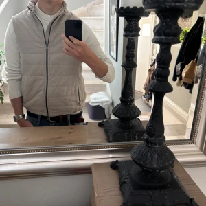 Beige quiltad väst Oscar Jacobson - Snygg beige quiltad väst från Oscar Jacobson med hög krage och dragkedja framtill. Västen har två fickor med dragkedja och diskreta knappar i nederkant bak. Skick 9/10 Inga defekter eller slitningar nypris cirka 3000 mitt pris 1399