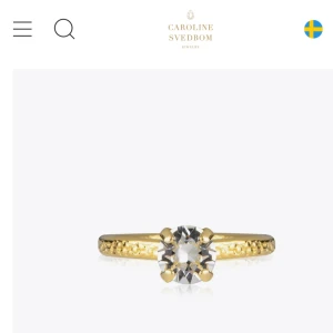 Guldring med klar sten Caroline Svedbom - Snygg guldfärgad ring från Caroline Svedbom med en stor, klar kristall i mitten. Ringen har en elegant och enkel design med en rund sten som verkligen glittrar. Perfekt för dig som gillar stilrena smycken med lite extra bling. Aldrig använd, nypris 395 🩷
