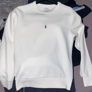 Vit sweatshirt från Polo Ralph Lauren  storlek xs / s  - Säljer en stilren vit sweatshirt från Polo Ralph Lauren med det klassiska blå logotypbroderiet på bröstet. Tröjan har långa ärmar och ribbade muddar vid ärmslut och nederkant. Perfekt för en avslappnad och snygg look.
