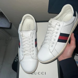 ÄKTA! Gucci ace  - Snygga vita sneakers från Gucci i skinn med klassiska blå och röda ränder på sidan. Hälpartiet har en metallicblå detalj med ormmönster och silverfärgad Gucci-logga. Skorna har rund tå, snörning och platt sula med unikt mönster undertill.
